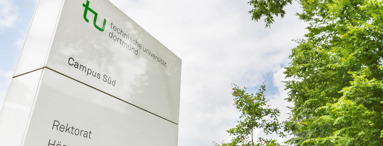 Hinweisschild Campus Süd Ein weißes Hinweisschild zum Campus Süd steht neben grünen Bäumen.